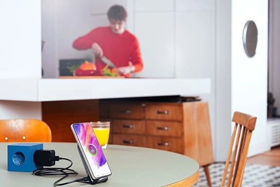 Un adolescente cocina al fondo, mientras un smartphone Samsung se carga sobre la mesa en la estación de carga inductiva.