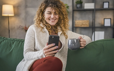 Una mujer se sienta en un acogedor sofá verde y utiliza su smartphone para controlar su casa inteligente.