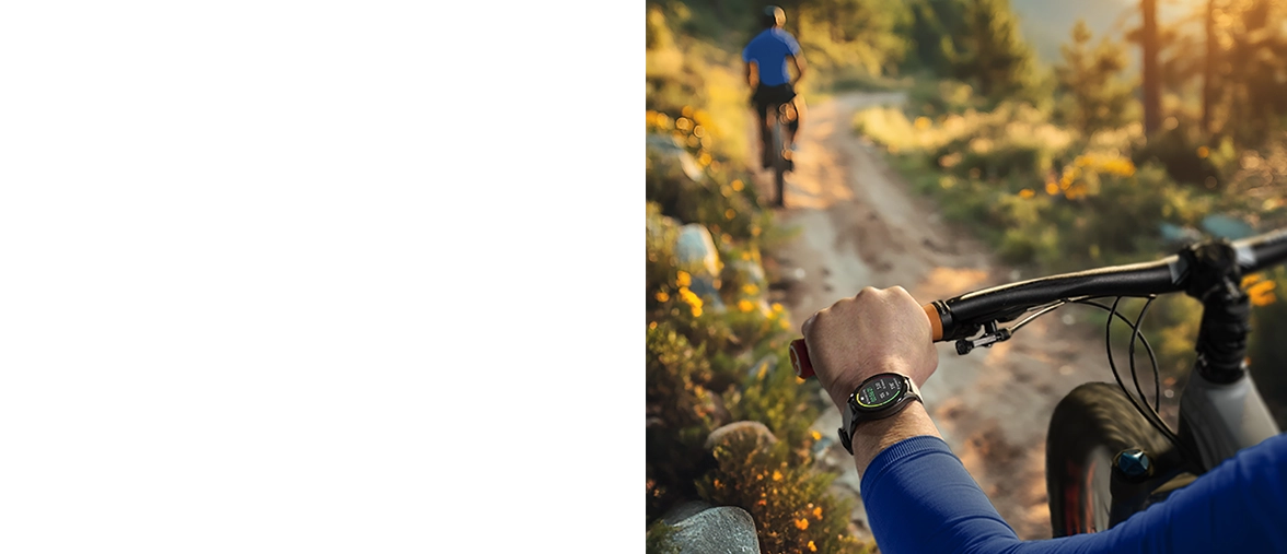 Vista por encima del hombro de un ciclista que circula por una carretera de grava rodeada de verdes prados, llevando un smartwatch Hama en la muñeca izquierda.