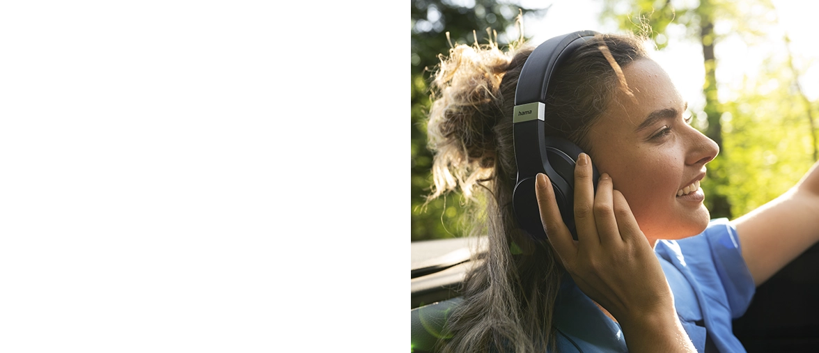 Una joven se sienta en un coche descapotable con los auriculares en los oídos y conduce por el bosque en verano.