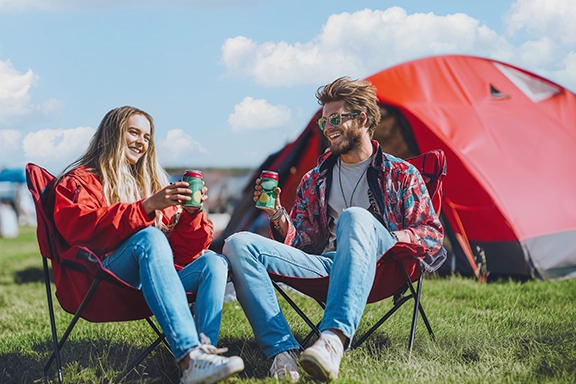 Dos amigos están sentados en tumbonas en el camping de un festival.