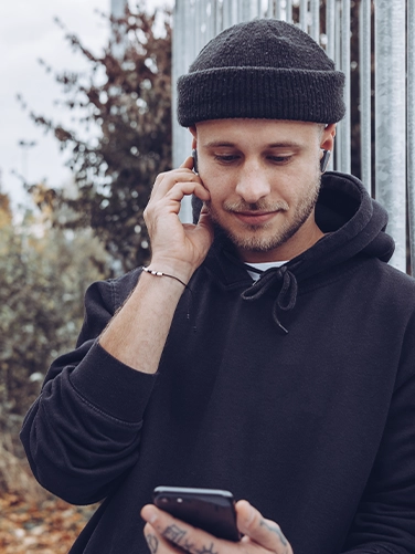 Joven con los auriculares Bluetooth «Spirit Pocket» de Hama y manejando su teléfono móvil.