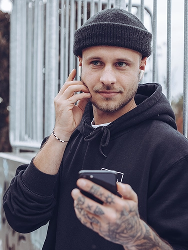 Joven con los auriculares Bluetooth «Spirit Pocket» de Hama y manejando su teléfono móvil.