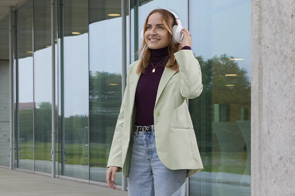 Una joven baja los escalones de piedra frente a un edificio llevando los auriculares Hama Bluetooth® «Spirit Calypso II»