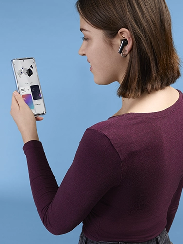 Mujer joven manejando su smartphone y realizando ajustes en los auriculares Bluetooth® «Passion Clear II» de Hama.