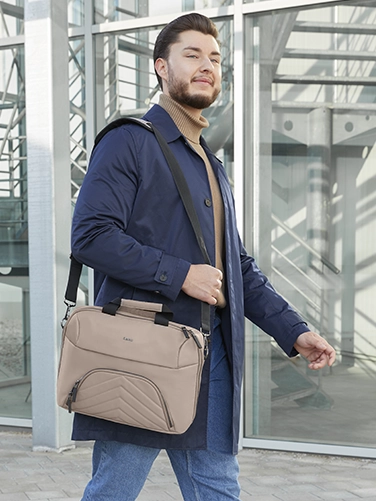 Un hombre de negocios lleva al hombro la bolsa para portátil "Premium Lightweight" de Hama de camino a la próxima reunión